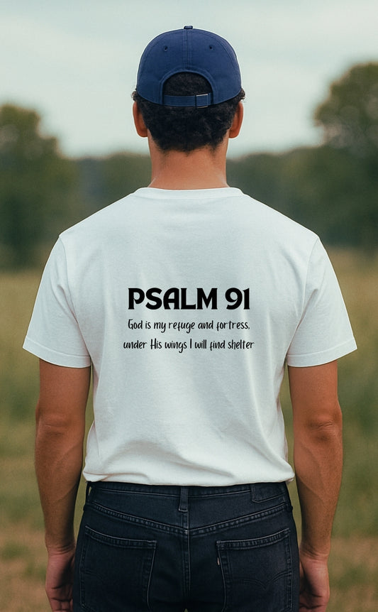 A young man wearing a white "Psalm 91 Code" Christian t-shirt from VerseWear by L'authority, seen from the back in a peaceful countryside setting. The shirt displays the Bible verse “Psalm 91 – God is my refuge and fortress, under His wings I will find shelter,” blending faith and style in a clean, minimalist design.
