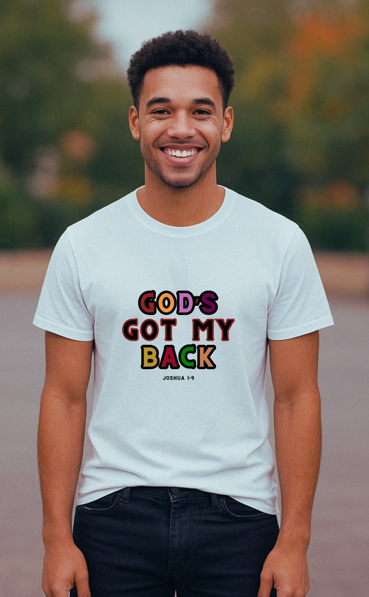 A young man wearing a white “God’s Got My Back” t-shirt by VerseWear by L'authority, featuring bold multicoloured text and the Bible verse Joshua 1:9. She stands confidently on a countryside path with green fields in the background, embodying strength, faith, and modern Christian streetwear.