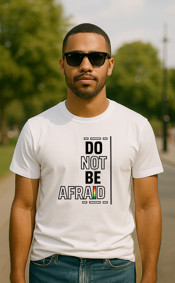 Man wearing white t-shirt from VerseWear by L’authority with bold vertical typography – 'Do Not Be Afraid' – featuring black text with red, yellow, and green accent in outdoor park setting