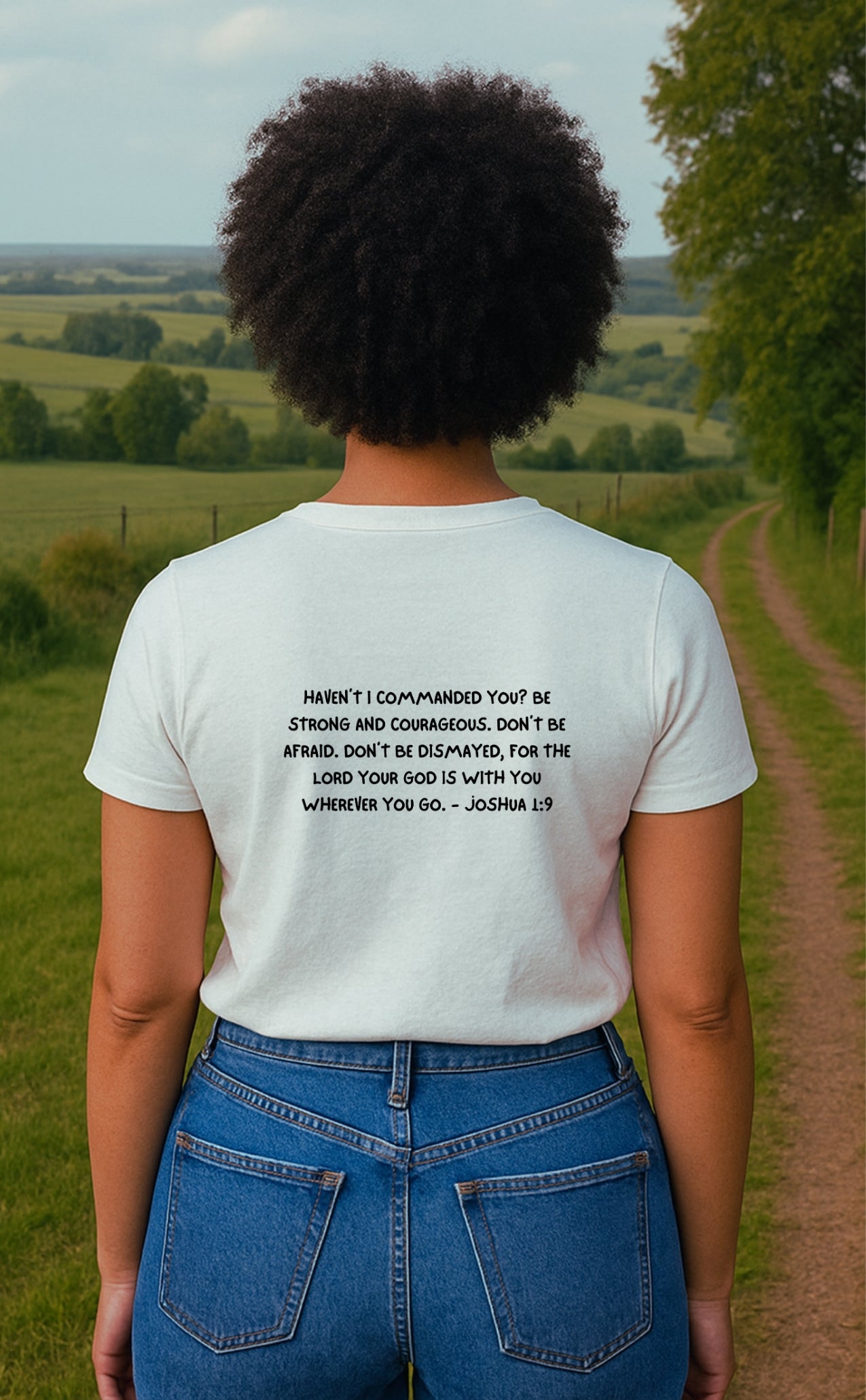 A young woman seen from the back, wearing a white Christian t-shirt by VerseWear by L'authority. The shirt features the full Bible verse Joshua 1:9 in bold black text: “Haven’t I commanded you? Be strong and courageous…,” delivering a powerful message of faith, strength, and divine assurance.
