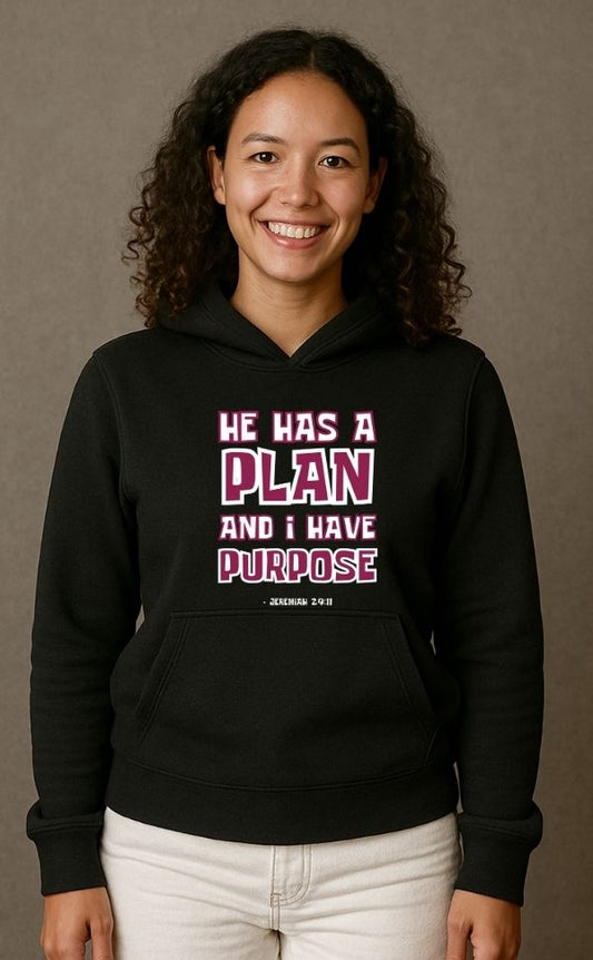 Smiling woman wearing black VerseWear by L'authority Christian hoodie with bold text 'He Has a Plan and I Have Purpose – Jeremiah 29:11' – inspirational faith-based streetwear.