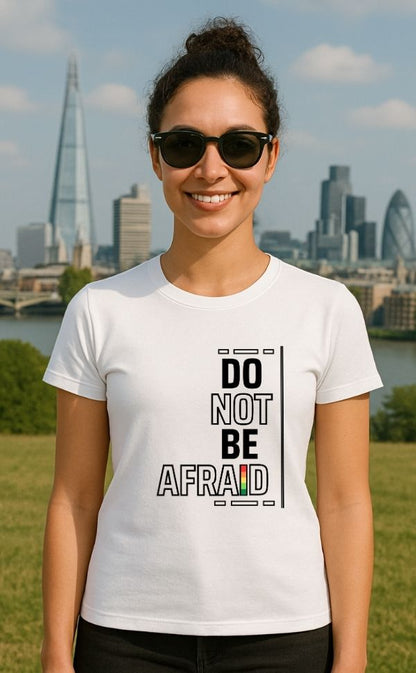 Smiling woman wearing white 'Do Not Be Afraid' t-shirt from VerseWear by L’authority with bold vertical typography – 'Do Not Be Afraid' – featuring black text with red, yellow, and green accent with London skyline in the background